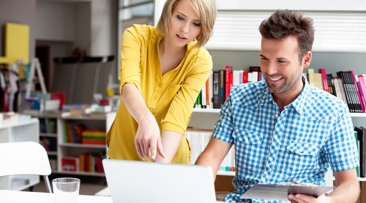 Two co-workers at the office discussing work on a laptop
