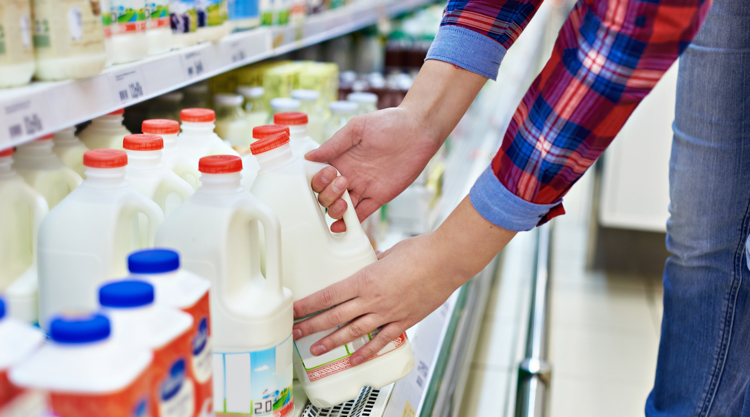 Photo of a person grabbing a gallon of milk at the grocery store