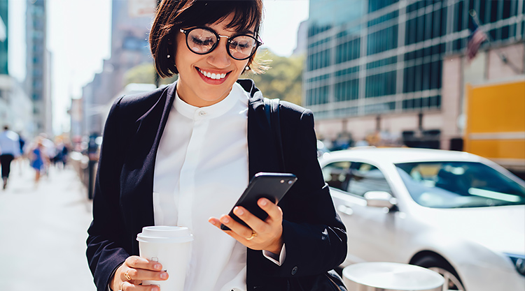 A smiling woman looking down at her cell phone while walking around outside
