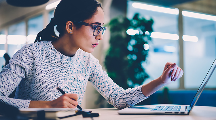 A woman seated at her desk with her laptop open in front of her in an office space
