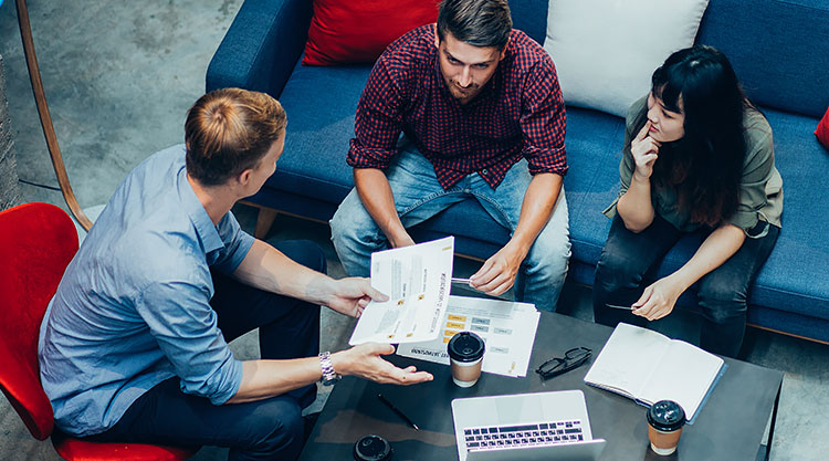 An overhead shot of three people seated on a couch going over files