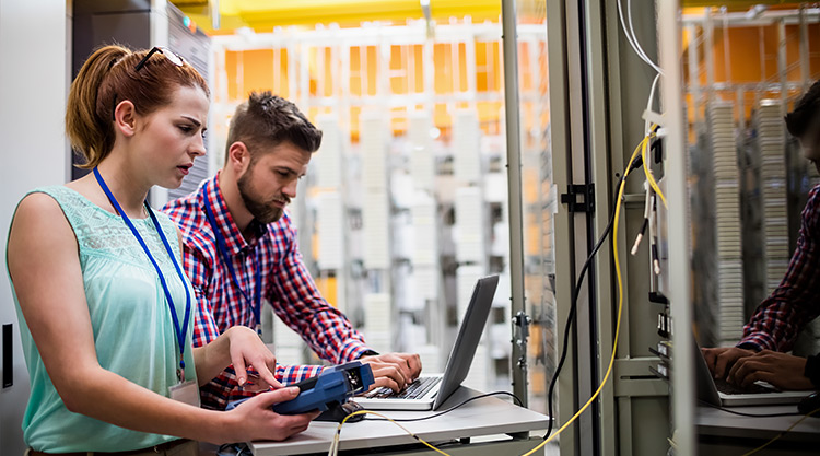 A woman and man standing near a laptop monitor with wires coming out of it