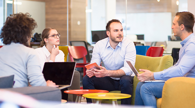 A group of employees seated together with their laptops open in an office space