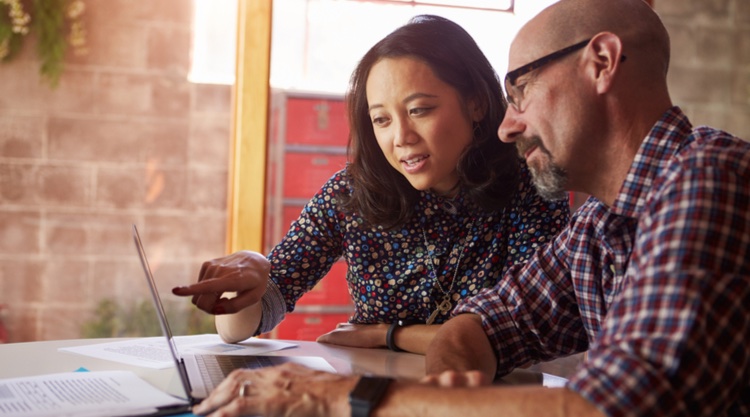 A woman and man looking at a laptop on their desk in an office space