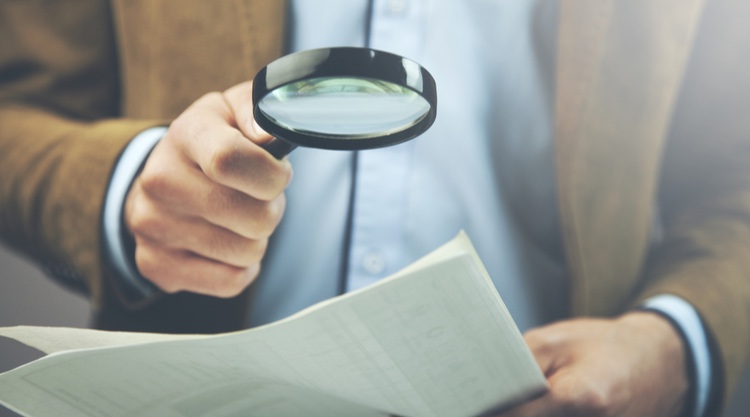 A man holding a magnifying lens over a handful of papers in his hand