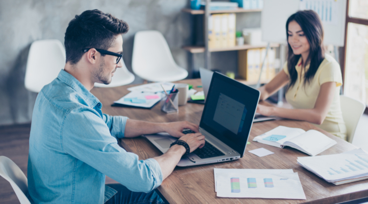 A man and woman are seated at a desk with paperwork around them