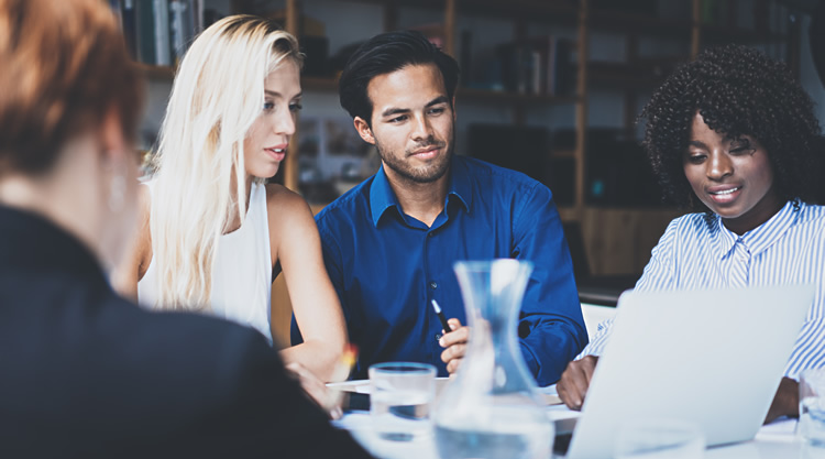 A group of people working in an office looking a laptop in the center