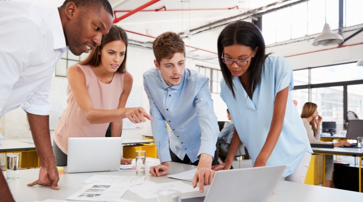 Four co-workers staring at the files and laptops on their desk while working in an office space