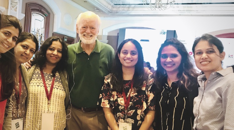 A group of smiling women and an older man stand together for a picture