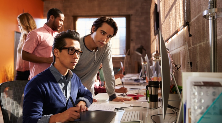 A group of employees huddled around a monitor in an office space