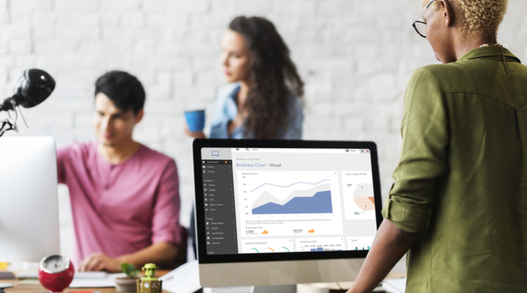 A woman standing in front of a computer monitor with two coworkers in front of her