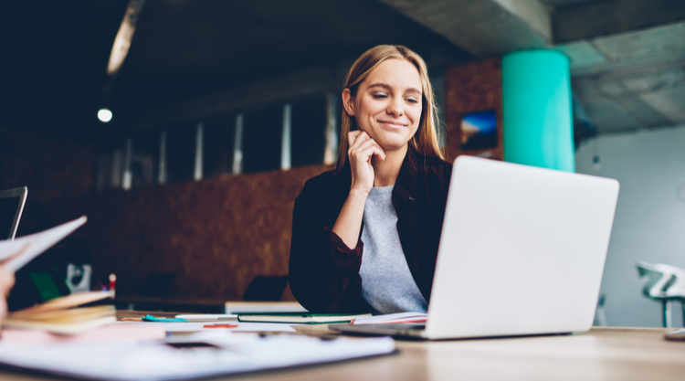 A woman smiling and working on her laptop in an office space