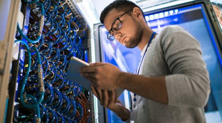 A man looking at a tablet in front of a wall of wires