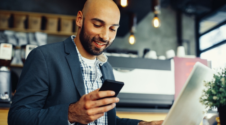 A man in a coffee shop working and looking at his cell phone