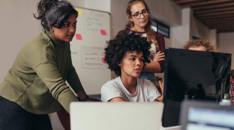Several women working in an office staring at a screen