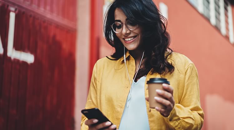 A woman holding a cell phone and mug while standing outside