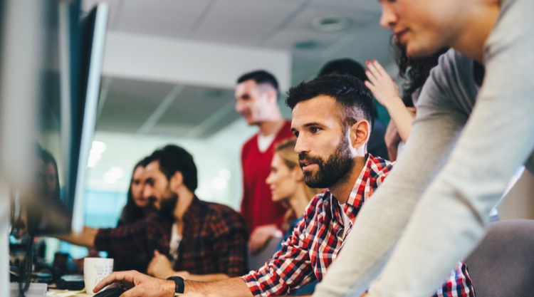 A man working in an office with his coworkers surrounding him