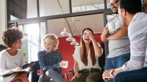 Four adults dressed in business work seated in a conference hall with their laptops open