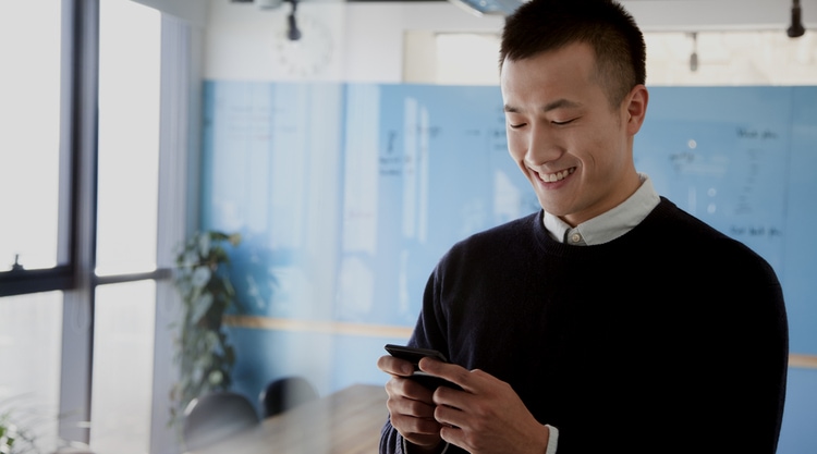 An adult man looking at the cell phone in his hand and standing in a well-lit office