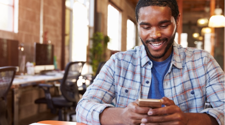 An adult man looking down at his cell phone in hand while sitting in a restaurant