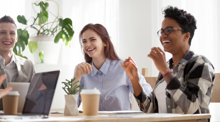 A group of coworkers laughing during a meeting and in an office