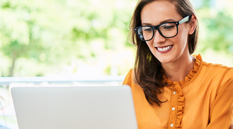 A smiling woman looking at her laptop sitting outside