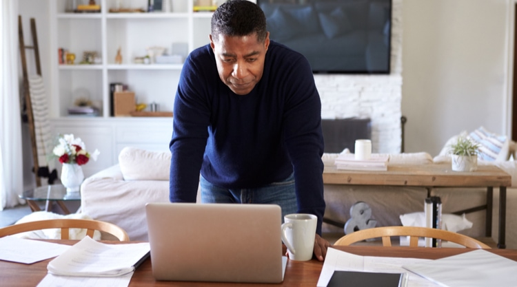 An older man leaning forward and looking at his laptop in his home
