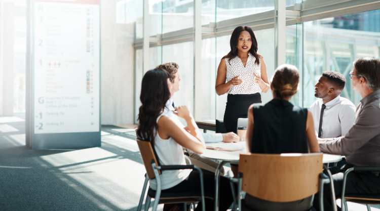A woman standing in front of a table of coworkers in an office