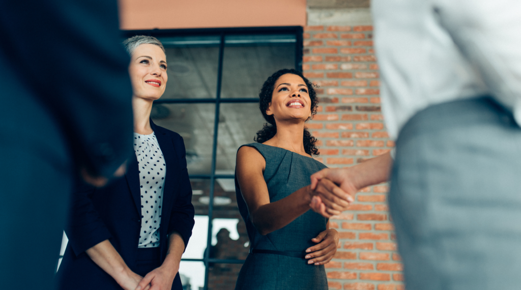 A woman shaking hands with another person and a older woman smiling next to her