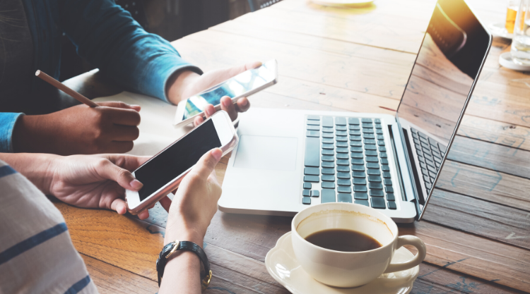 Two people holding cell phones and working in a cafe