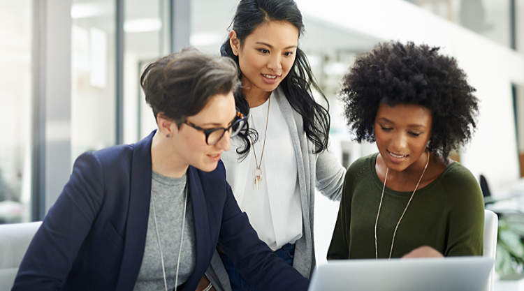Three women working in an office and looking at the laptop in front of them