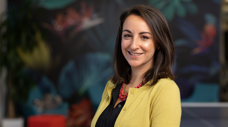 Smiling adult woman looking straight ahead and standing in front of a flower mural in an office