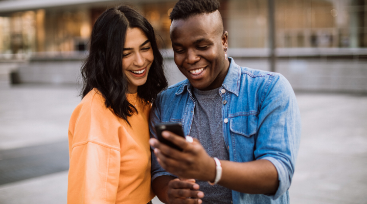 A man holding his cellphone and a woman standing next to him looking at the screen while standing outside
