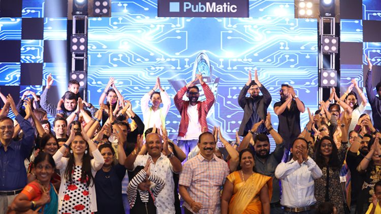 A crowd of smiling people standing outside with a stage that stays PubMatic behind them