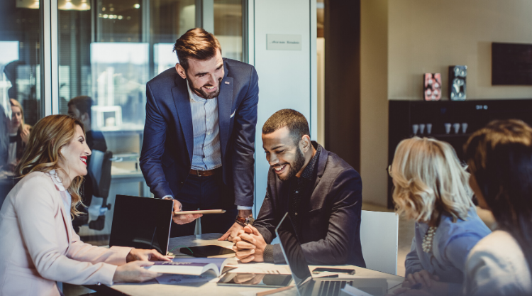 A group of coworkers sitting at a conference table smiling and looking their work material