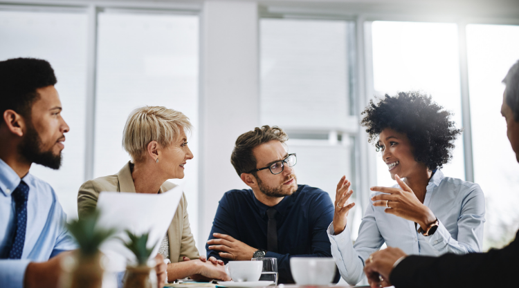 A woman in a meeting speaks to a crowd of coworkers as they all listen