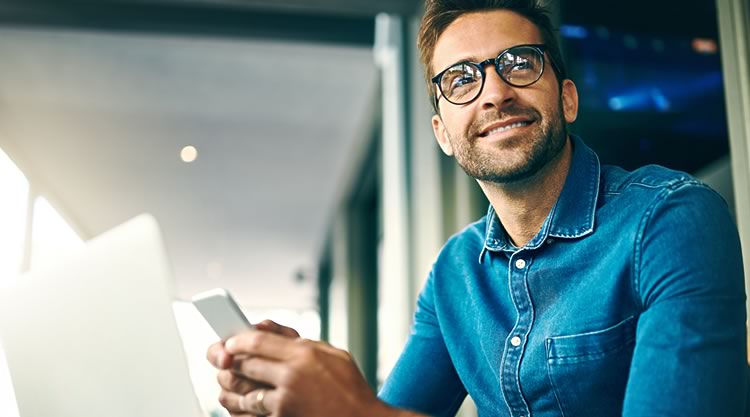 A seated man holding a cell phone looks forward