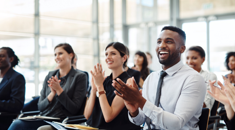 A crowd of seated smiling professionals clap