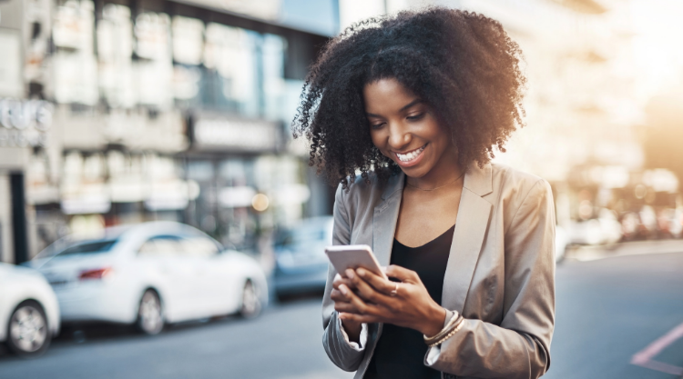 A smiling young woman looking at her cell phone standing in the road