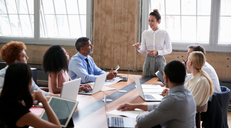 A woman standing in a conference room with a crowd of people seated ad listening.