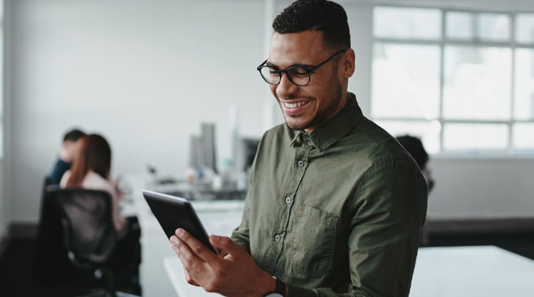 A young man holds a tablet while standing in an office
