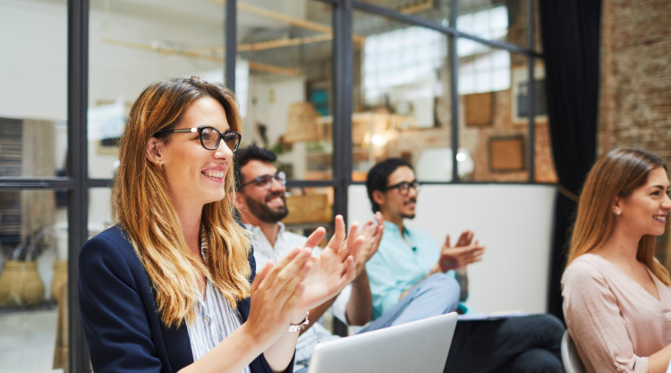 A small crowd of professionals claps as they listen to a presentation