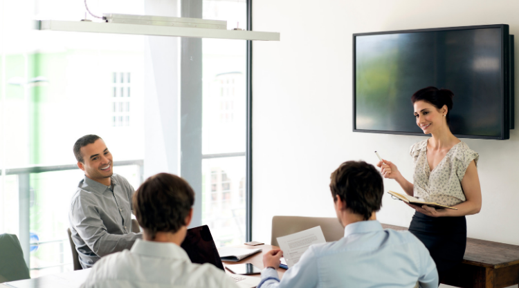 A woman stands in a conference room amongst her coworkers