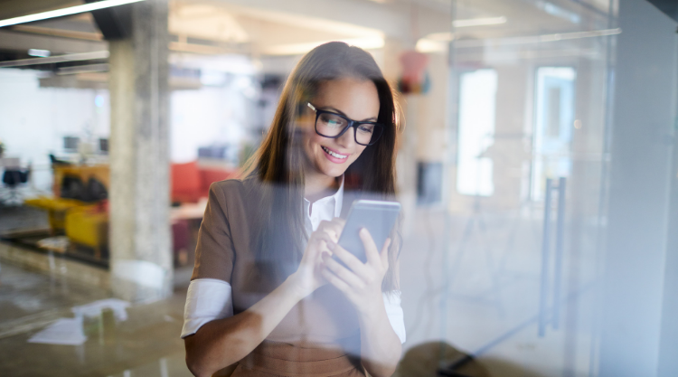 A smiling woman looks at her tablet while standing in her office