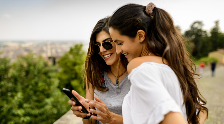 Two women hiking look at the cell phone in their hands.