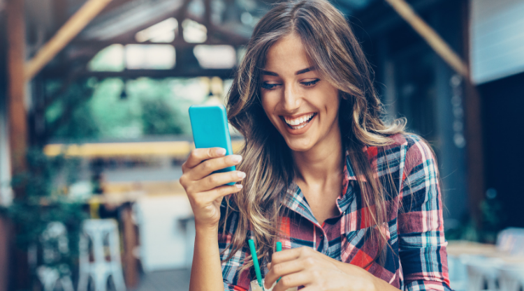 data providersA laughing woman looks into her cell phone while seated outside.