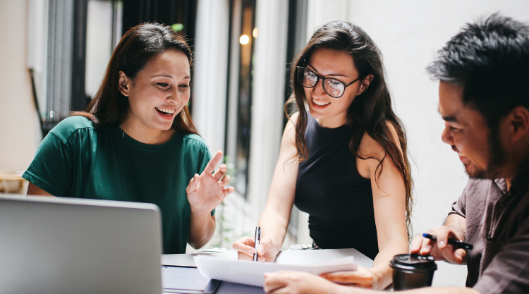 Three smiling adults sitting in an office space and working on a project together