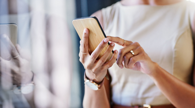 A woman holding a cell phone standing near a window.