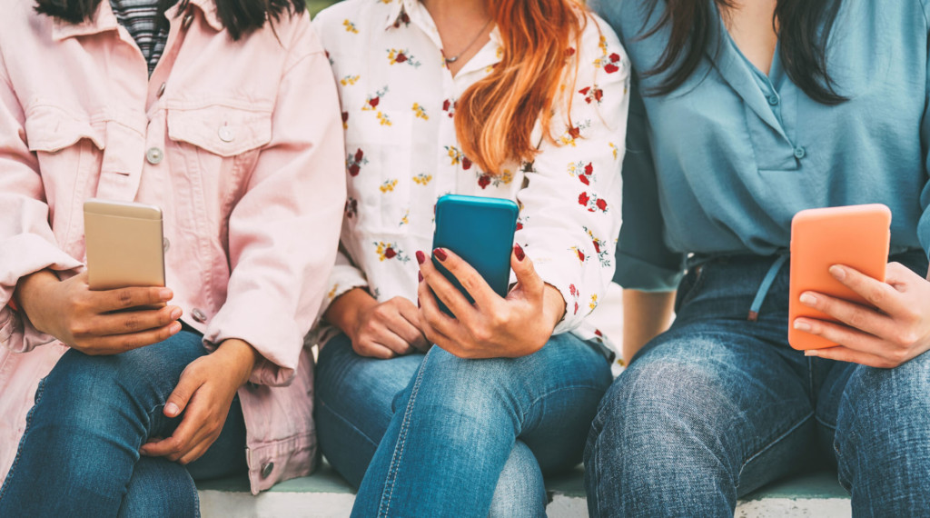 Three women sit by each other with a cellphone in hand