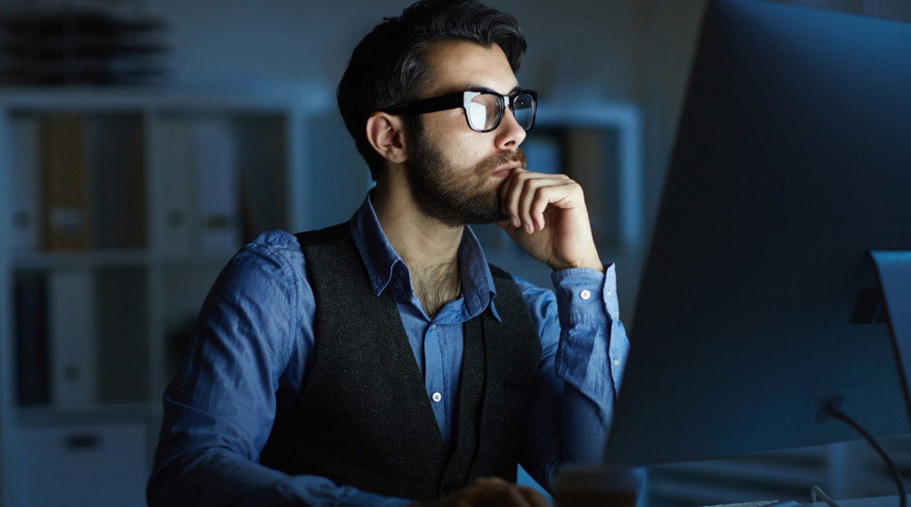A man in a dark room stares into a computer screen